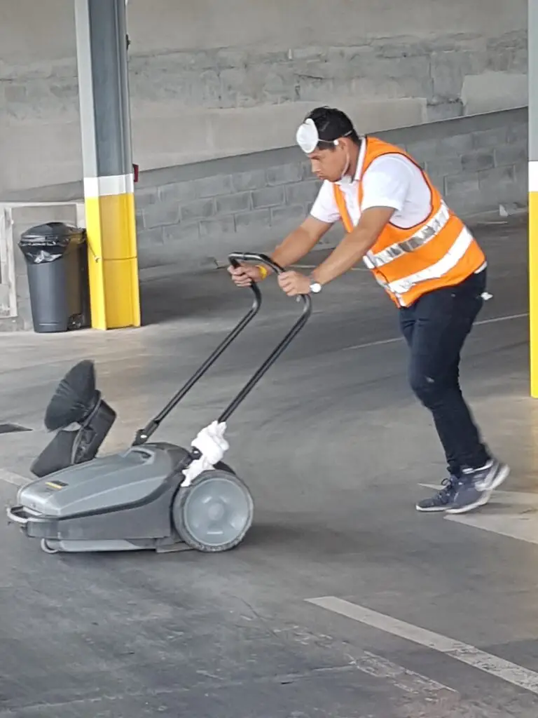 Conserje limpiando un estacionamiento con una barredora industrial